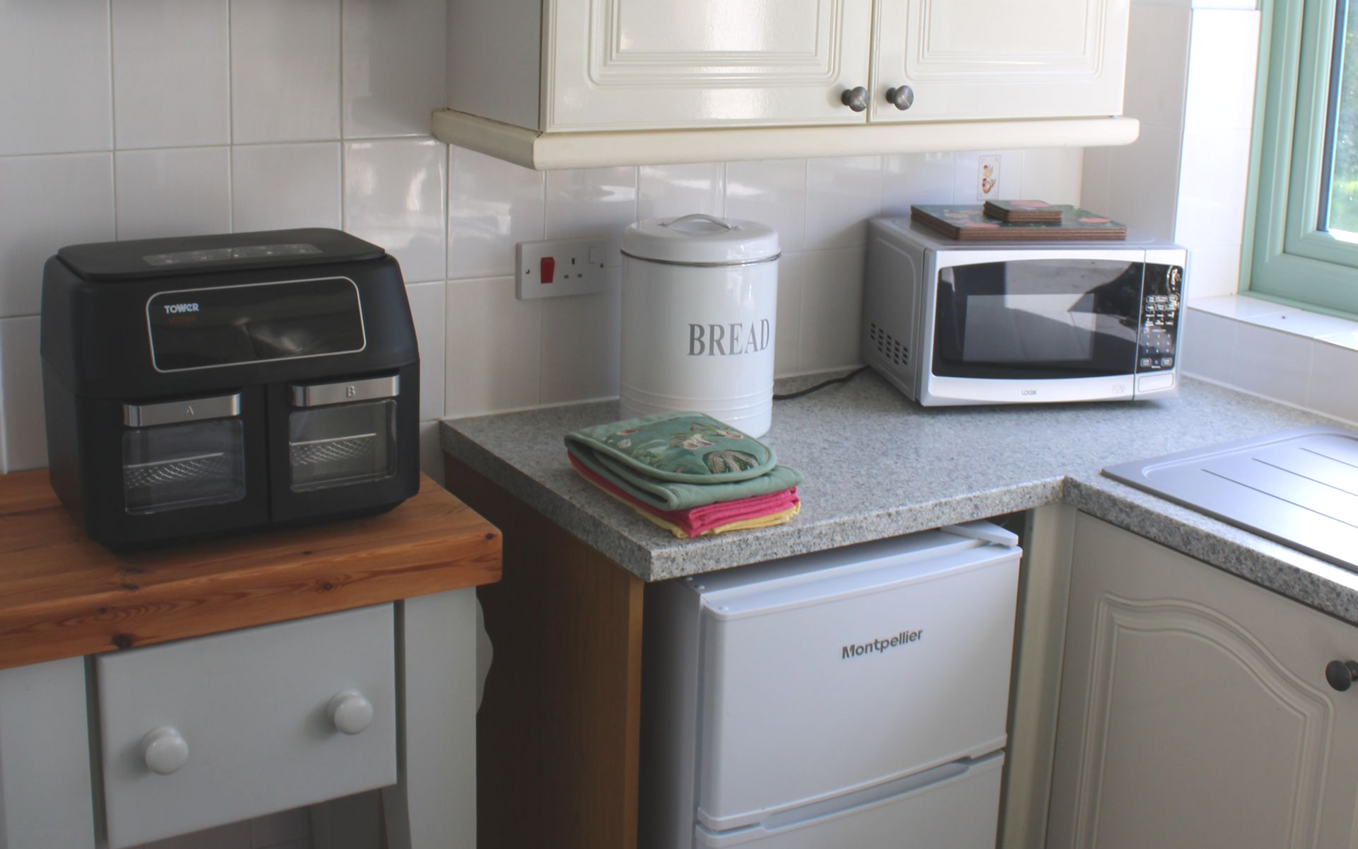 Small kitchen counter with toaster oven, microwave, coffee maker, and mini fridge under white cabinets.