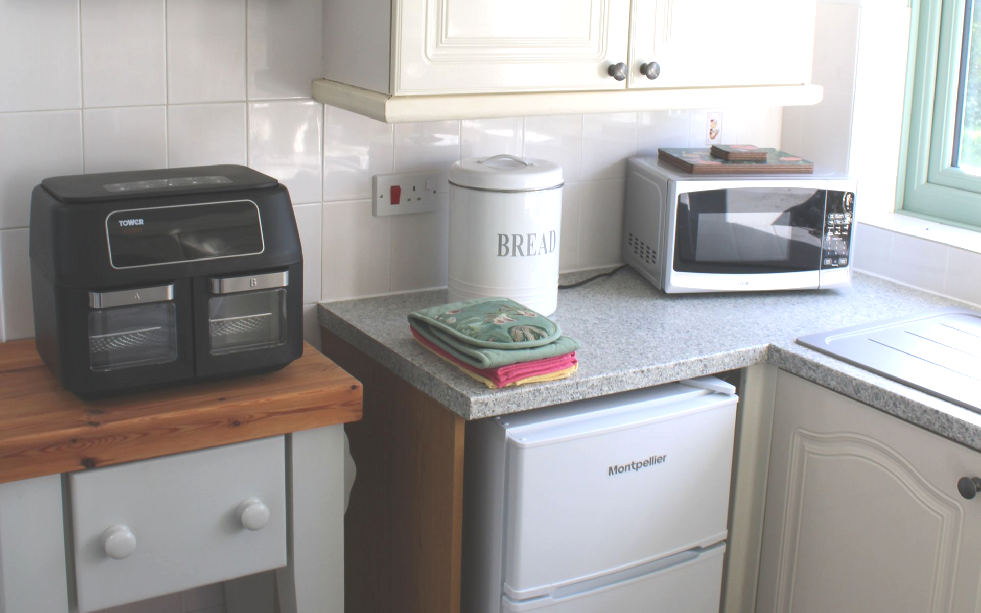 Kitchen counter with toaster oven, coffee canister, microwave, and mini fridge under white cabinets.
