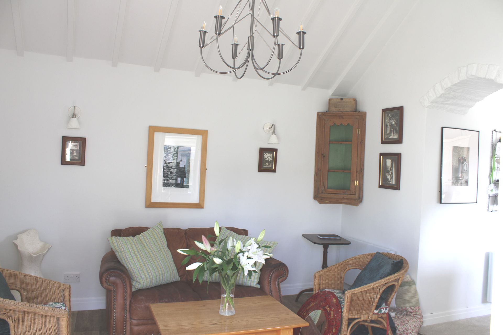 Cozy white-walled living room with wicker chairs, sofa, coffee table, chandelier, and framed wall art