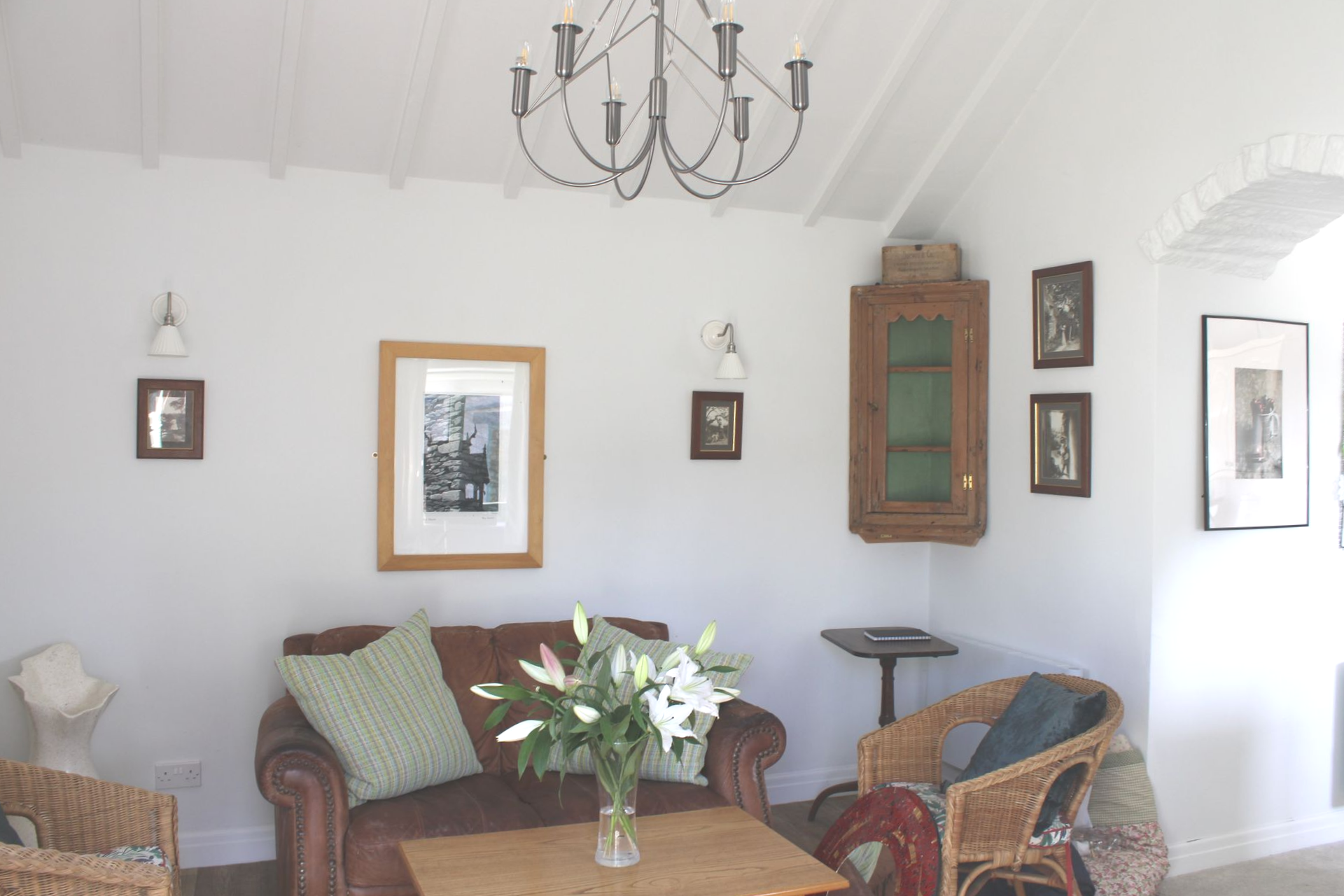 Bright living room with wicker chairs, sofa, coffee table, wall art, and chandelier