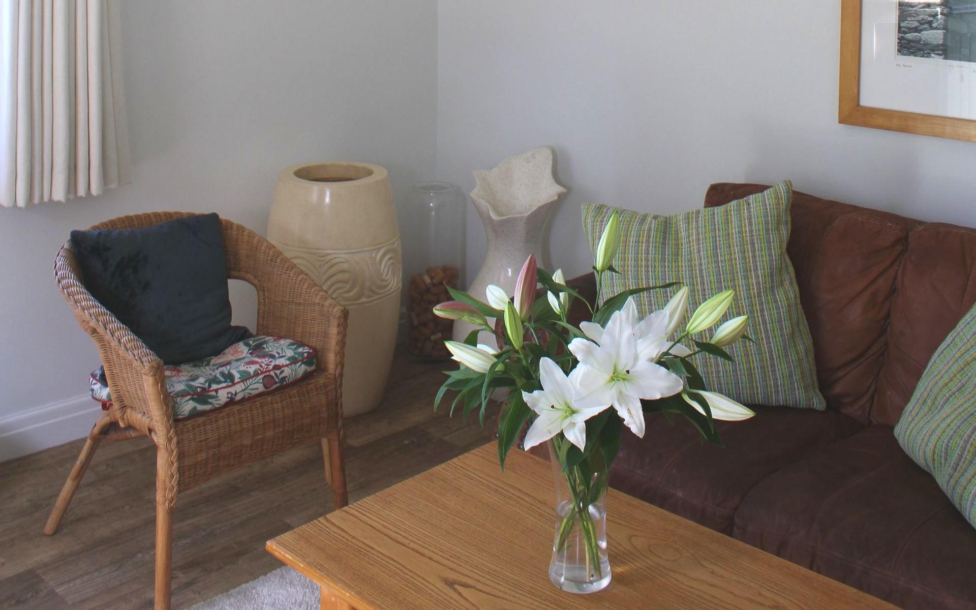 Cozy living room with wicker chair, brown sofa, and coffee table holding a vase of white lilies