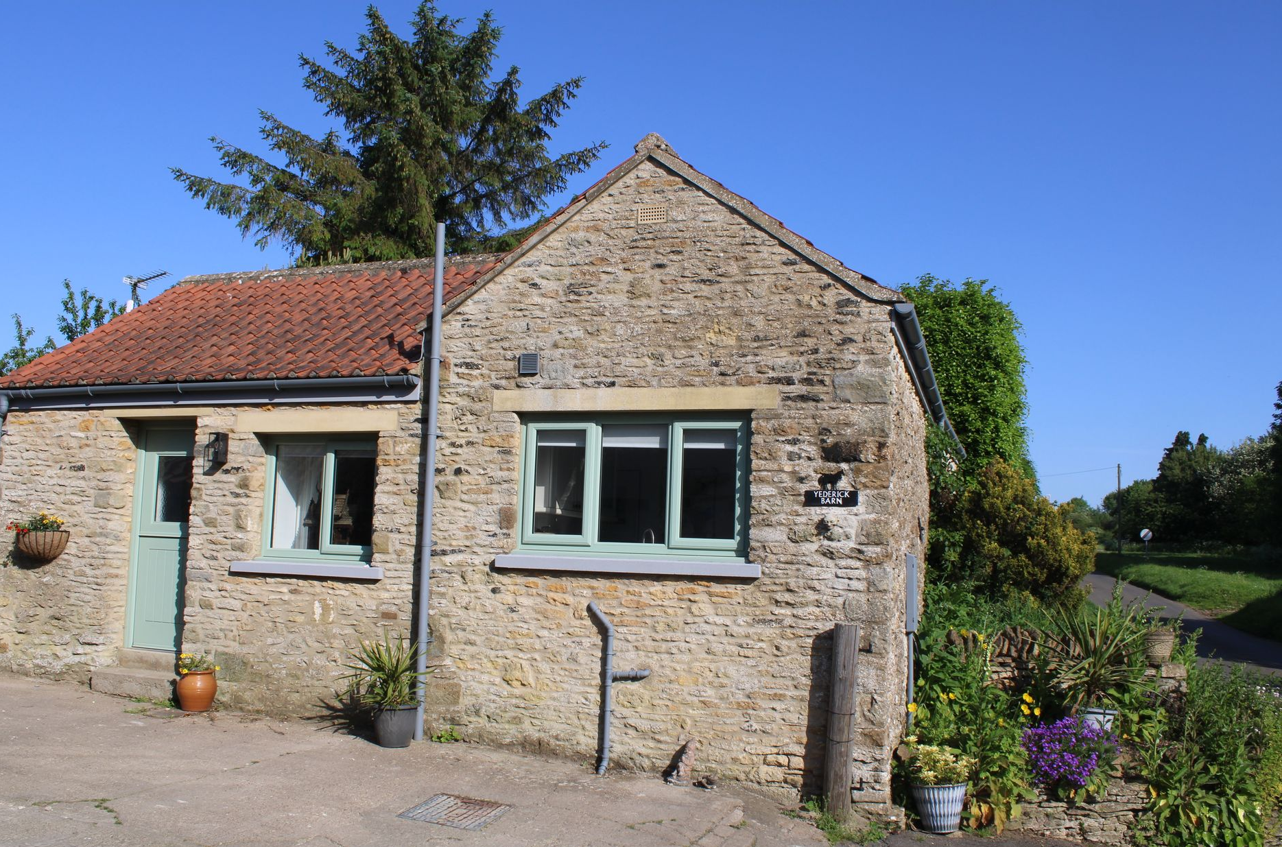 Stone cottage with red-tiled roof, green shutters, and a blue sky in the countryside