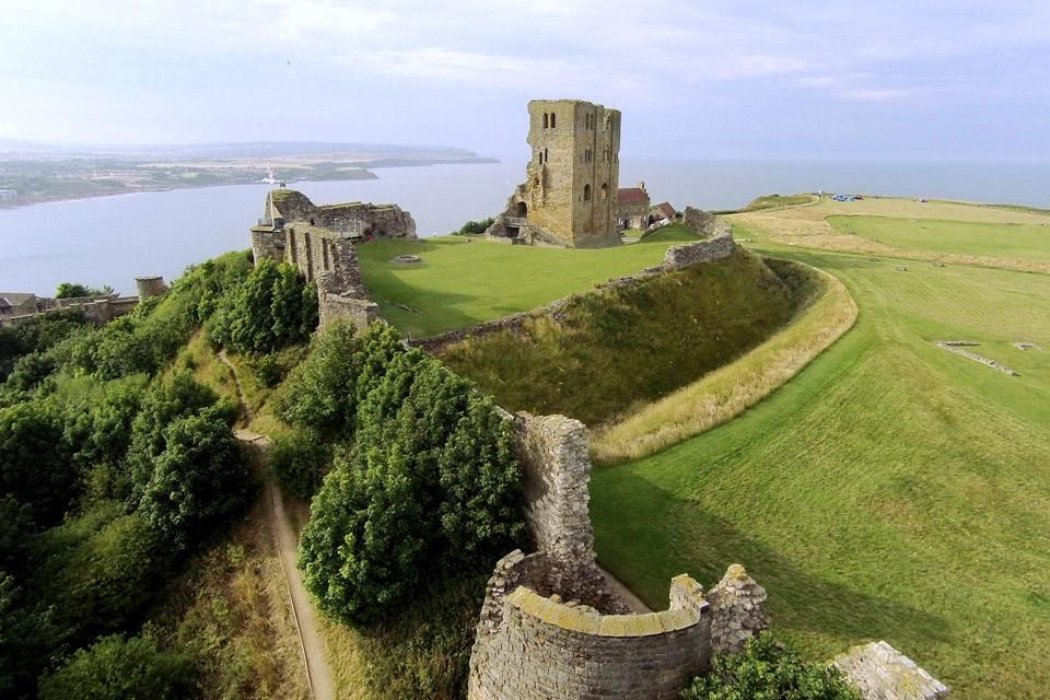 Ruined stone castle on a grassy cliff overlooking the sea under a hazy sky