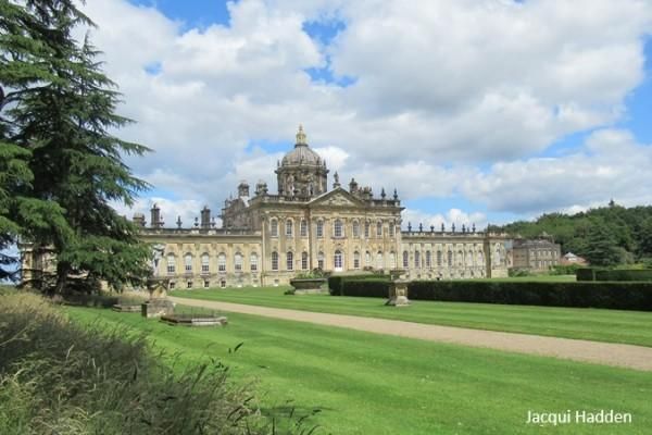 Grand historic palace with domed roof, long facade, and manicured lawn under a cloudy sky.