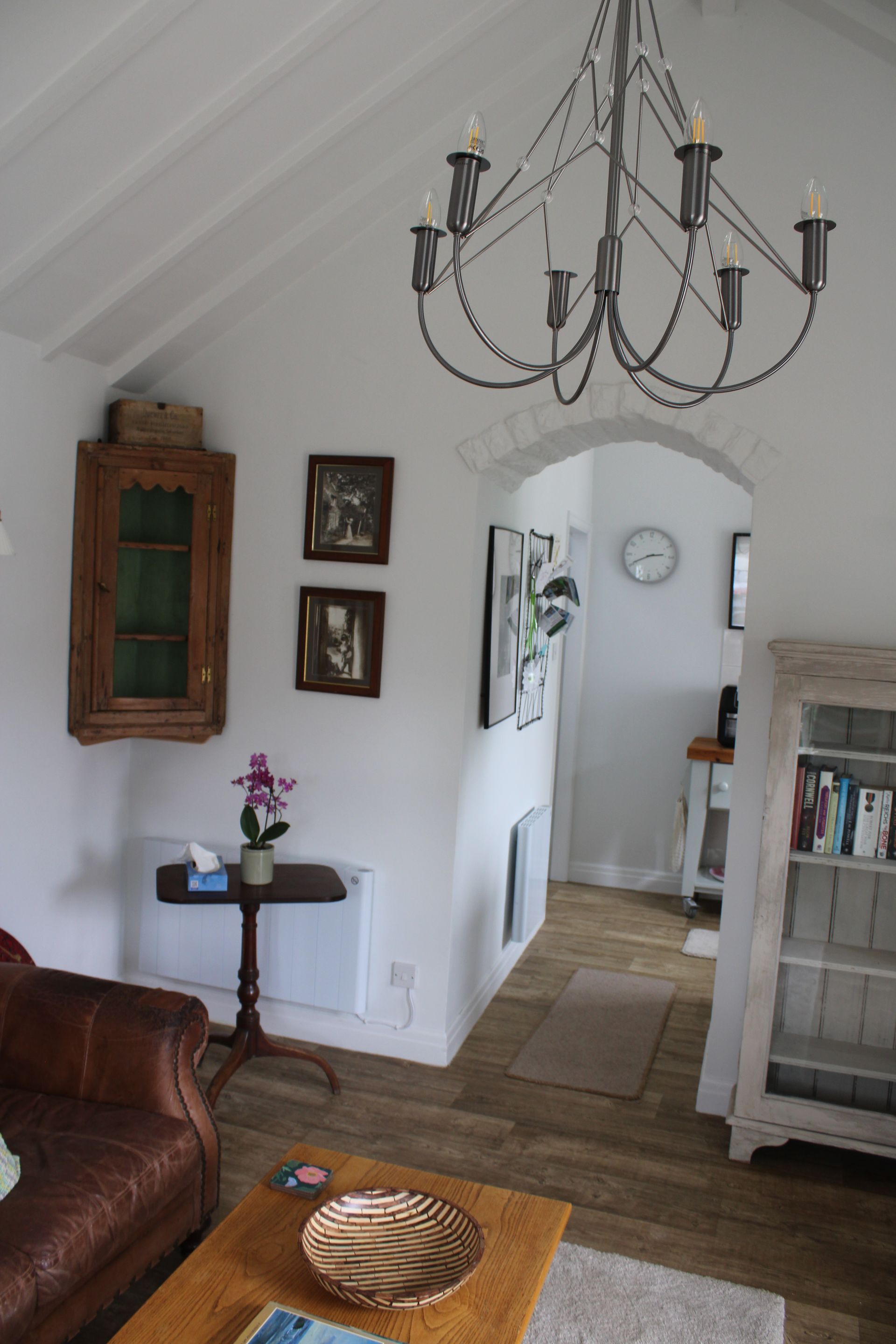 Cozy living room with white walls, chandelier, brown sofa, and an arched doorway to a hallway