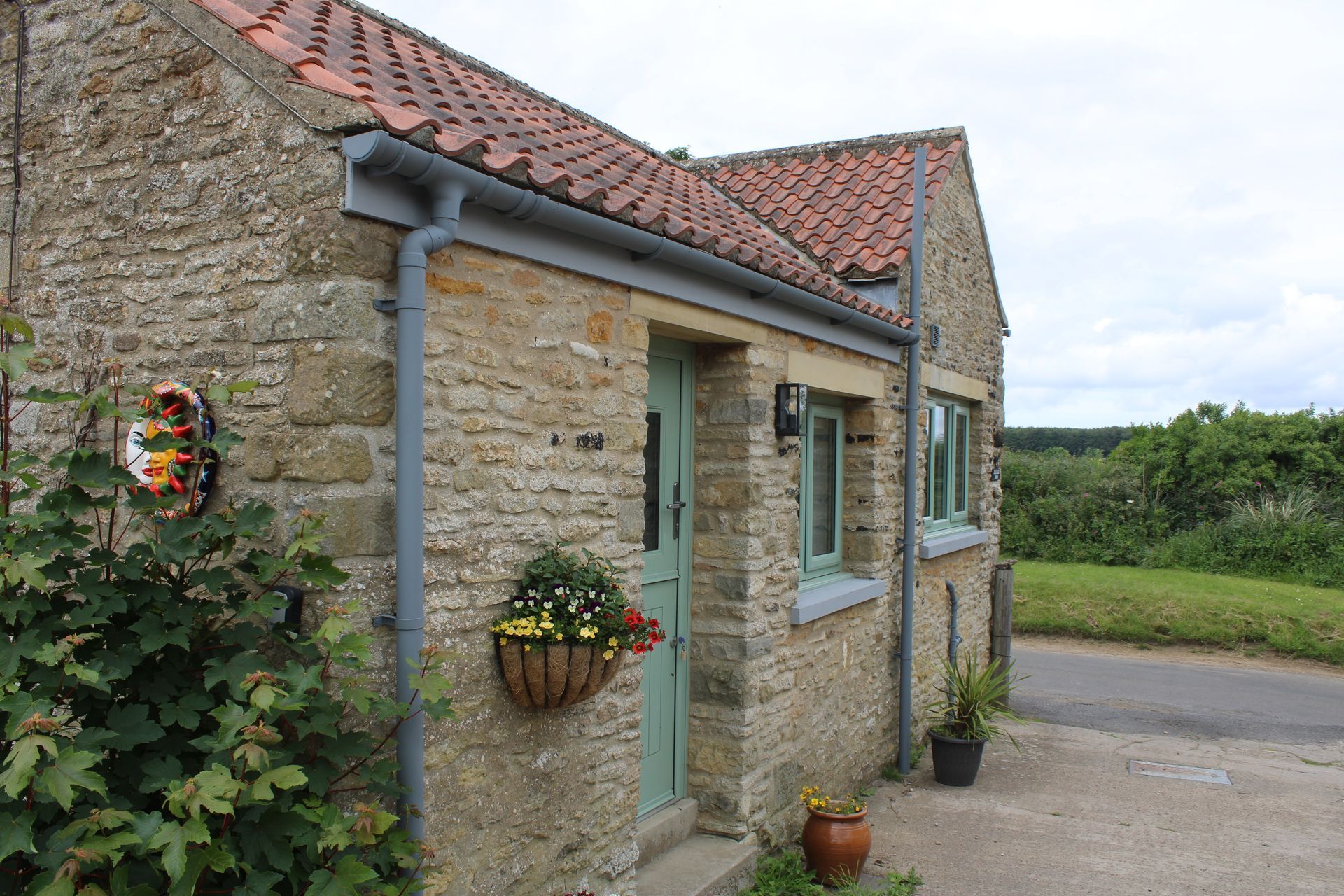 Stone cottage exterior with red-tiled roof, turquoise door and window trim, and hanging flower baskets