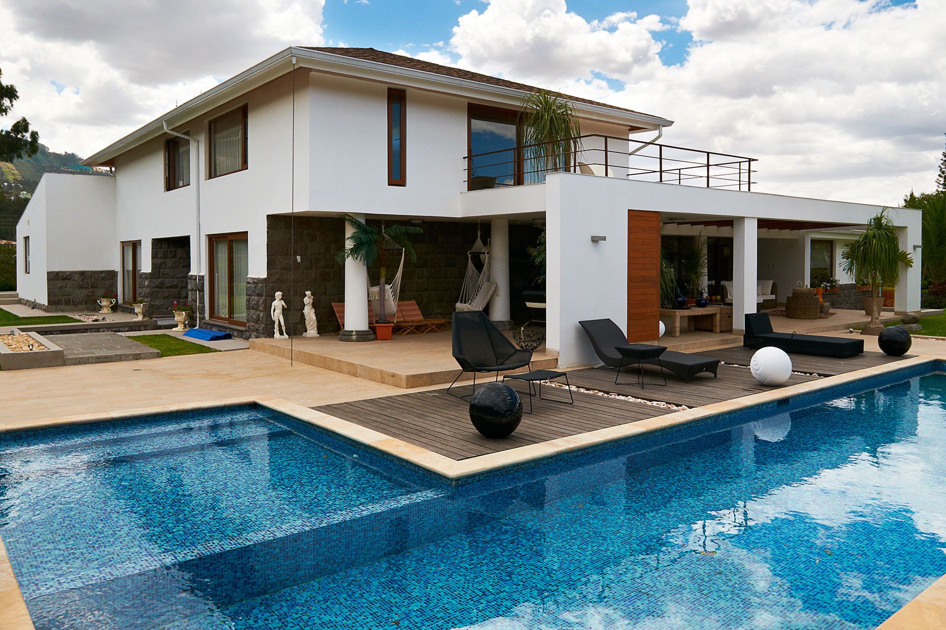 Modern white house with a pool. Features a pool, patio with lounge chairs, and balcony. Blue sky.