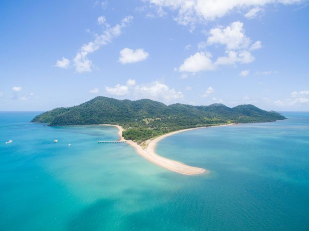 Aerial view of a tropical island with lush green vegetation and a sandbar surrounded by turquoise water.
