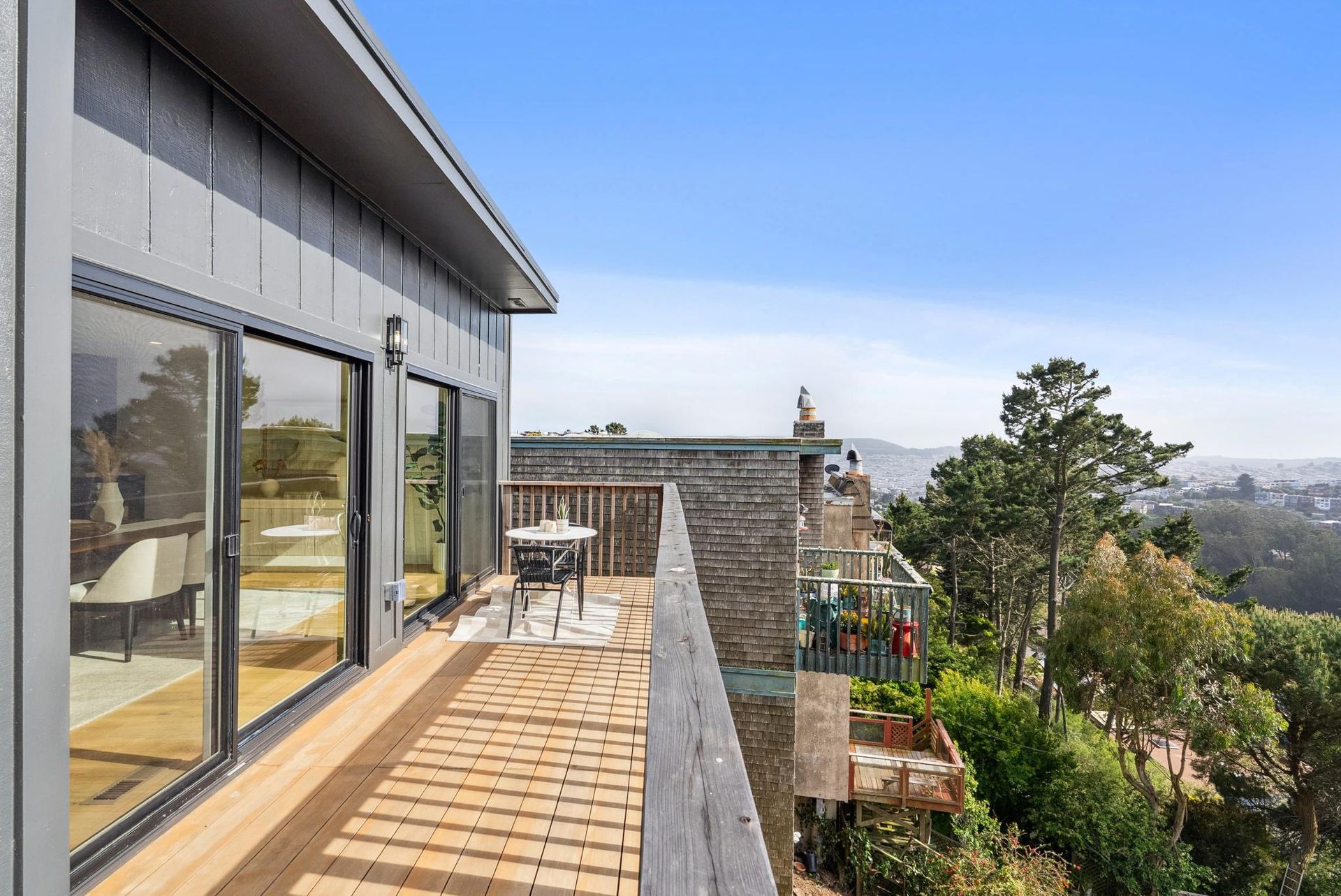 Deck of a house overlooking trees and a distant cityscape under a blue sky.