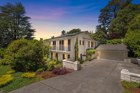 Two-story home with white stucco walls, balcony, and attached garage. Driveway, lush greenery, and sunset sky.