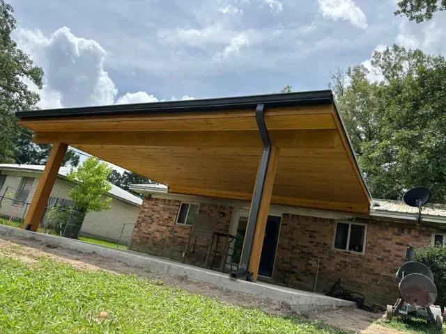 Covered patio/carport with wood ceiling and brick house under a cloudy sky