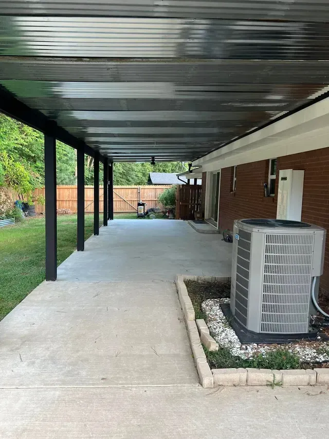 Covered concrete patio with air conditioner units beside a brick house and lawn.