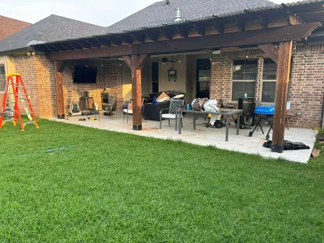 Backyard patio with brick house, covered seating area, grill, and bright green lawn