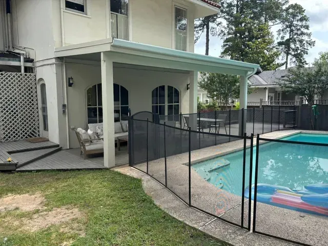 Backyard pool area beside a house with a covered patio and black safety fence