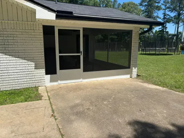 Screened patio entrance beside a concrete driveway and grassy yard at a house