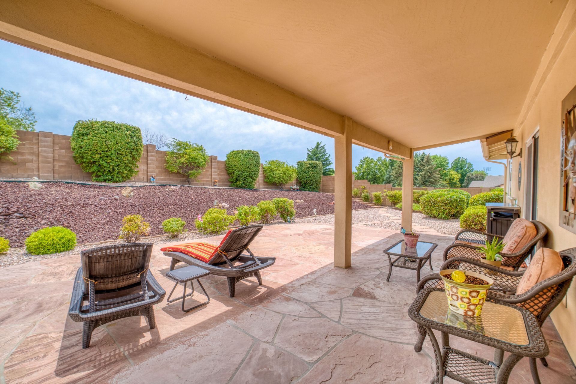 A patio with a cover featuring several chairs overlooking a lush backyard landscape.
