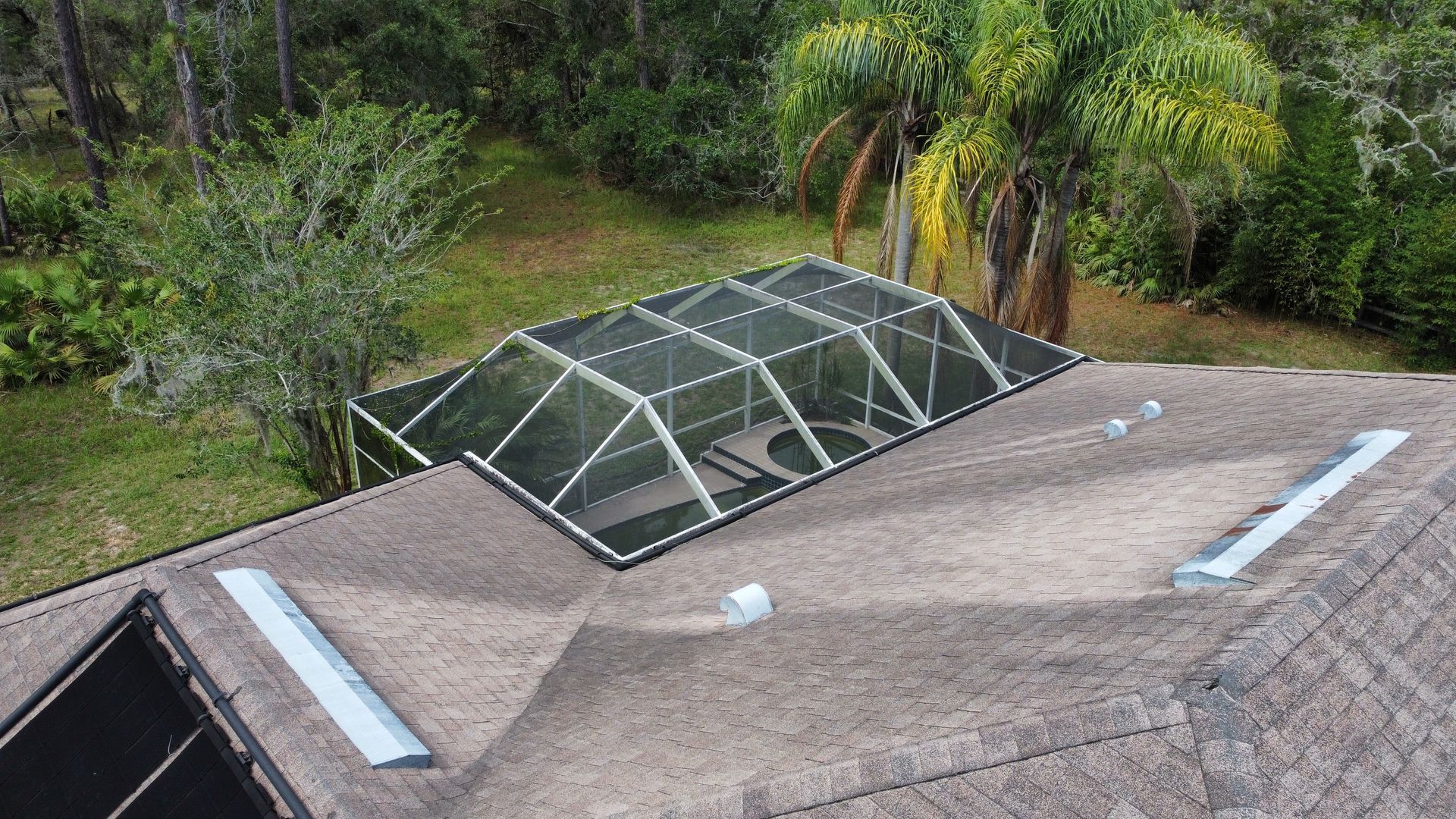 Aerial view of roof with screened pool enclosure surrounded by trees and greenery.