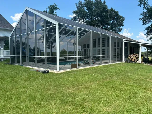 Glass-enclosed sunroom with a white frame beside a grassy lawn under a blue sky