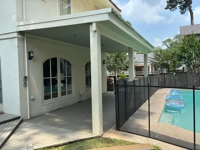 Backyard patio beside a fenced swimming pool with a covered porch and white columns