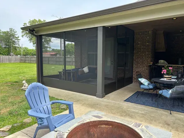 Covered patio with screened porch, blue chair, fire pit, and outdoor seating beside a grassy yard