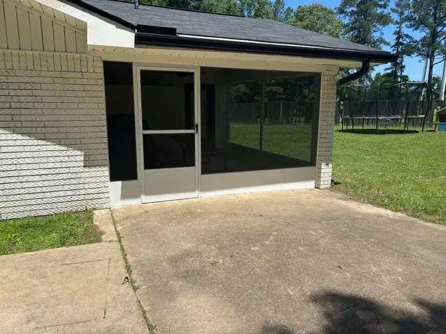 Screened patio entrance beside a concrete walkway and grassy yard on a sunny day