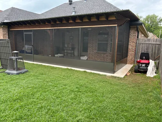 Backyard patio with screened porch, green lawn, and a small red lawn tractor beside the house