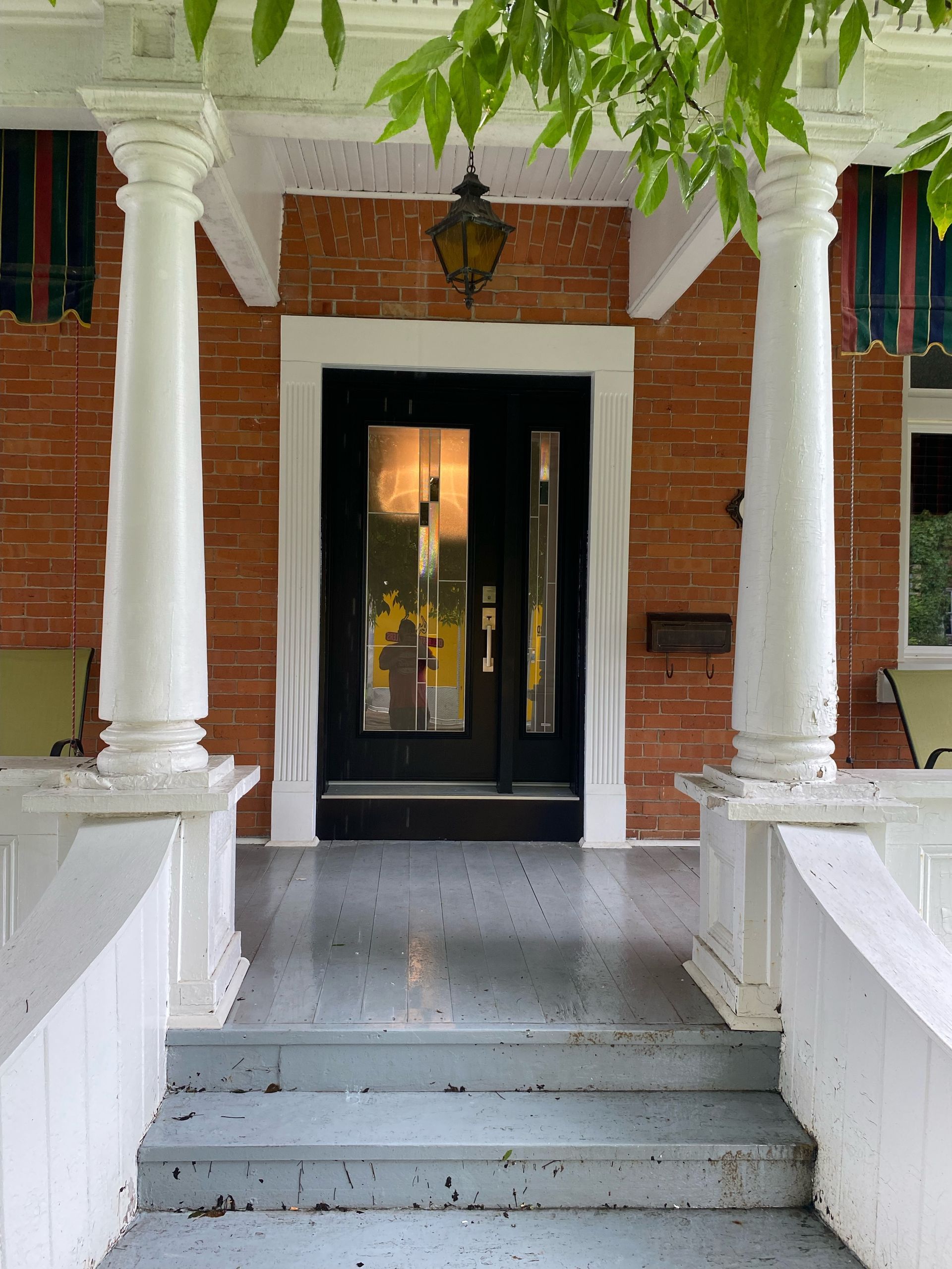 Front porch with white columns, brick wall, black front door, and steps leading up to the entrance.