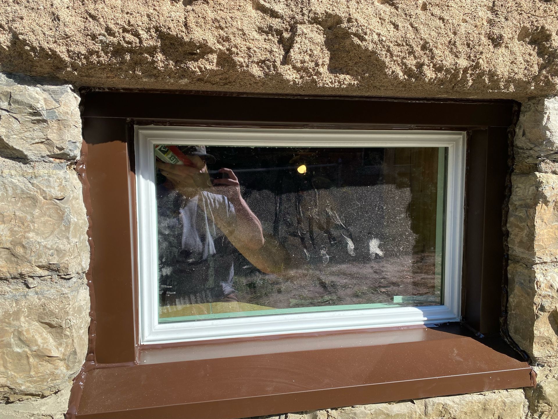 Small basement window set in a stone wall with a brown frame and reflective glass.
