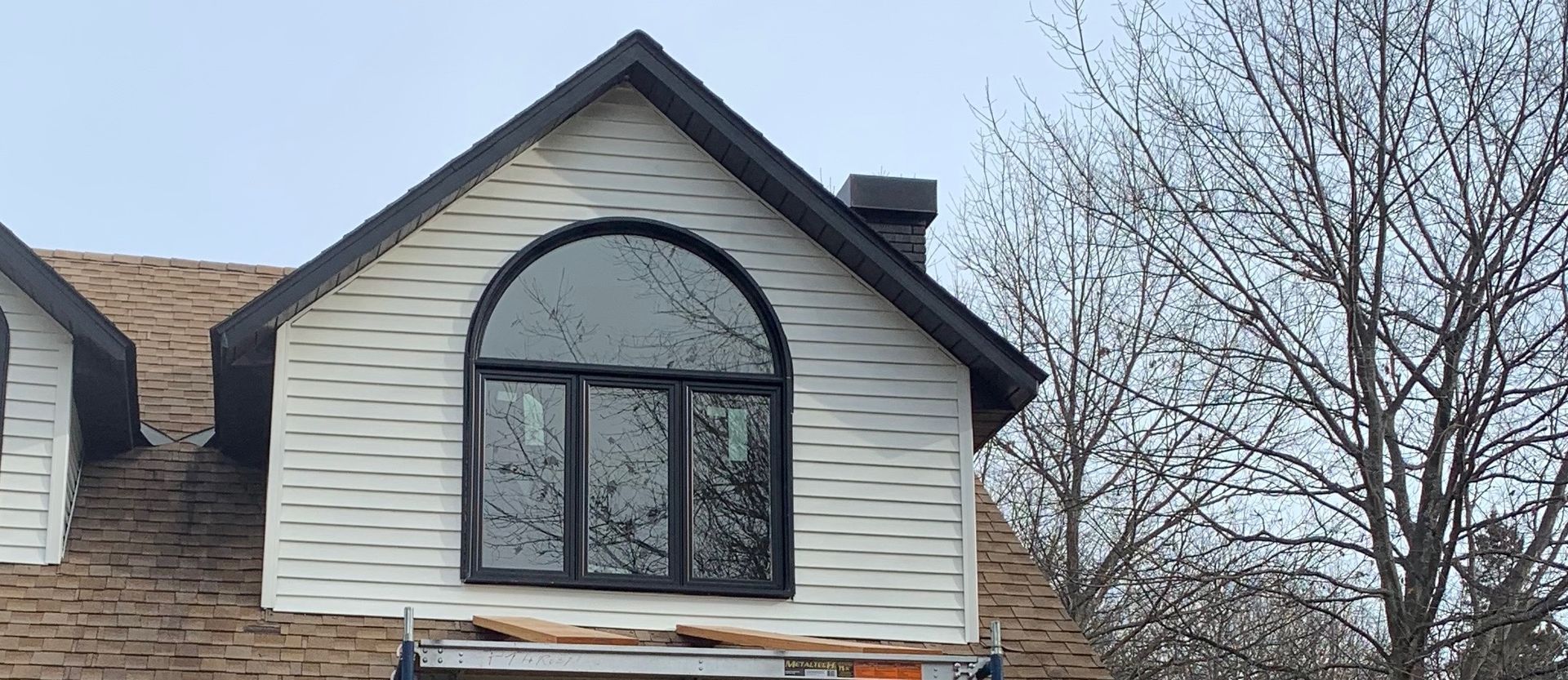House exterior with a dormer window, white siding, and a bare tree beside it