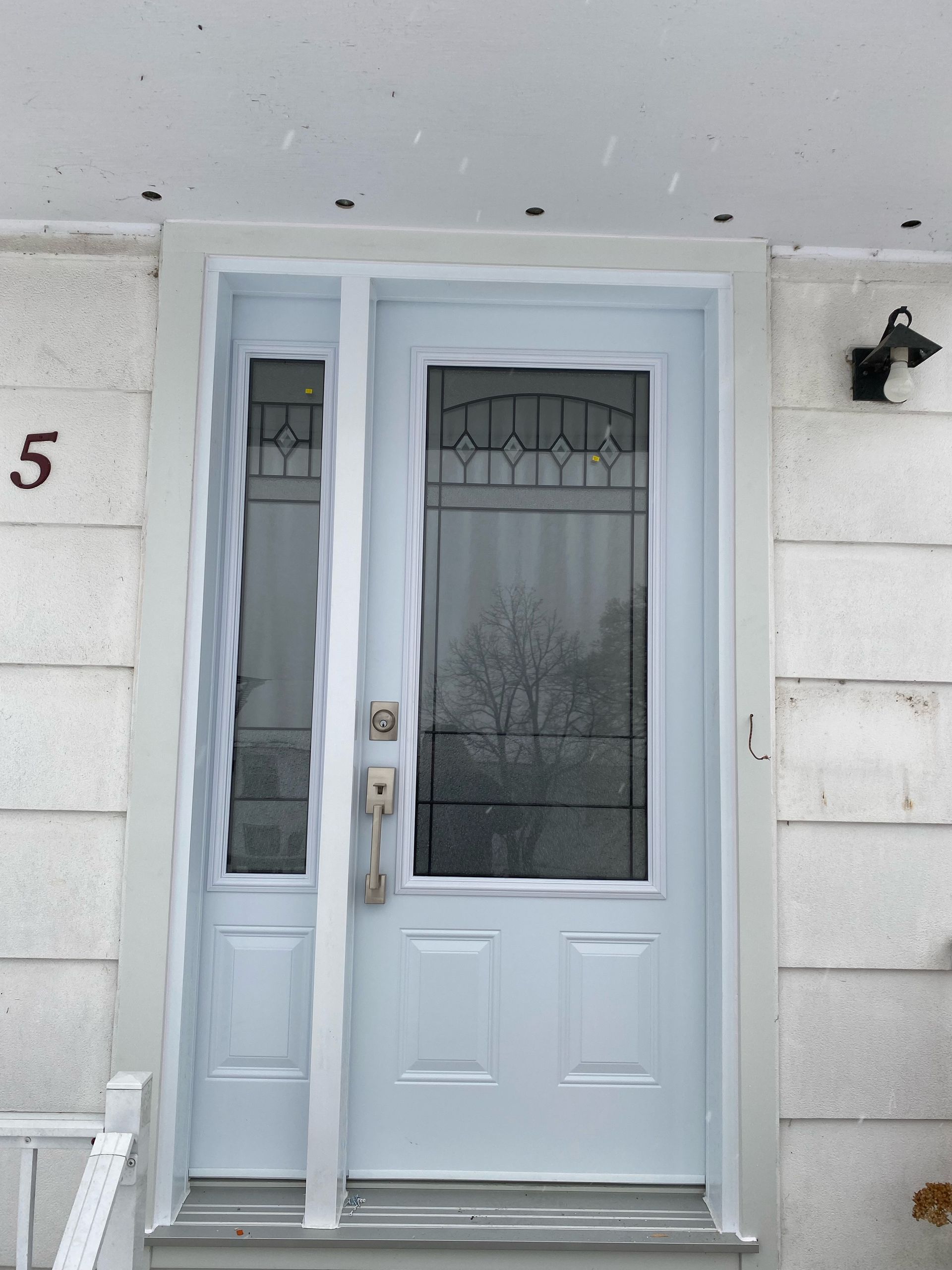 White front door with glass panels and a side window on a light gray house.