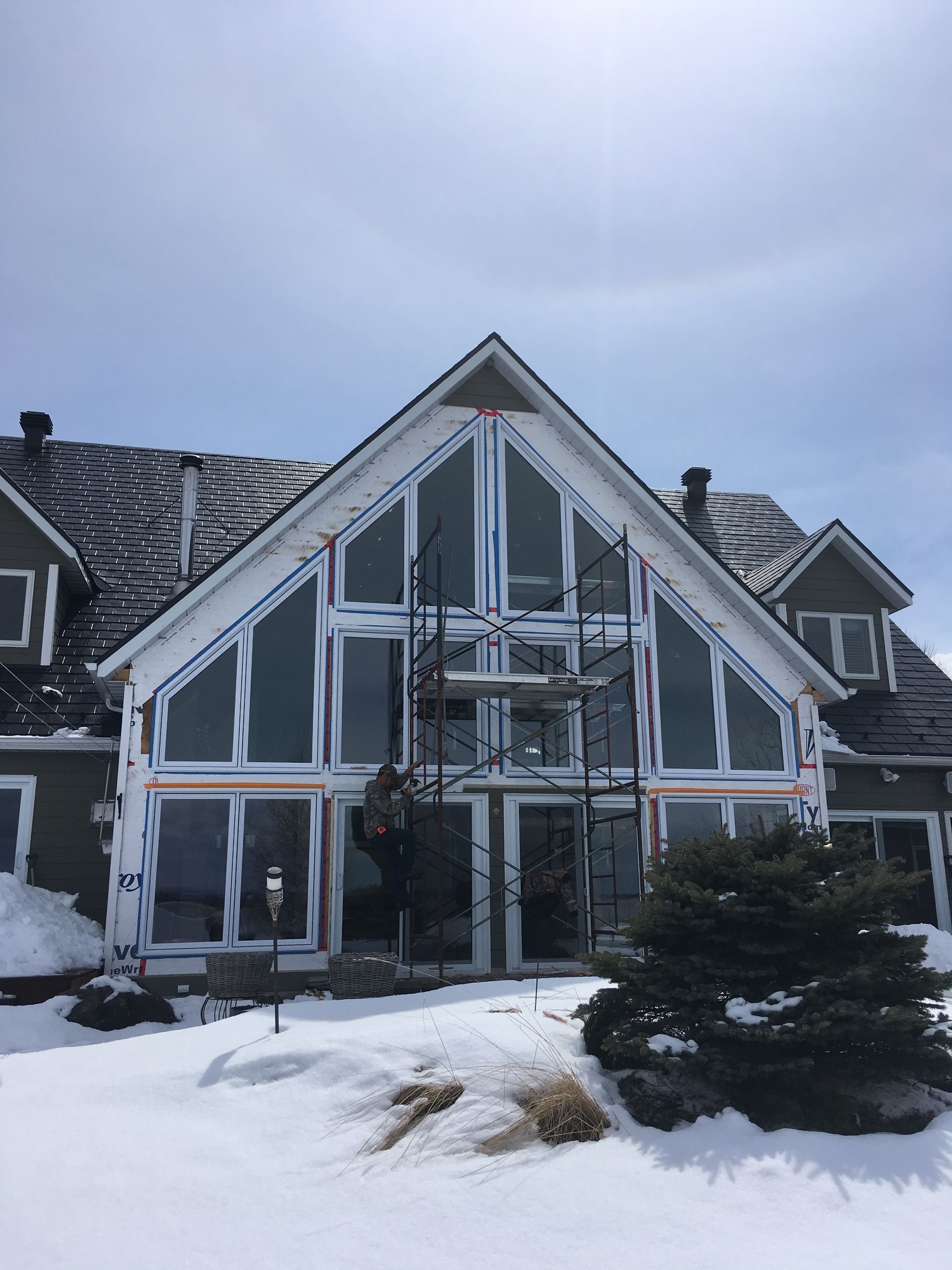 Snowy modern house with a steep gabled roof and front porch under a cloudy sky