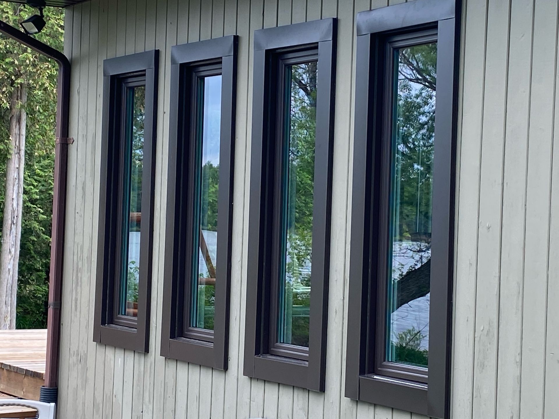 Four dark-framed windows in a light wood exterior wall reflecting trees outside