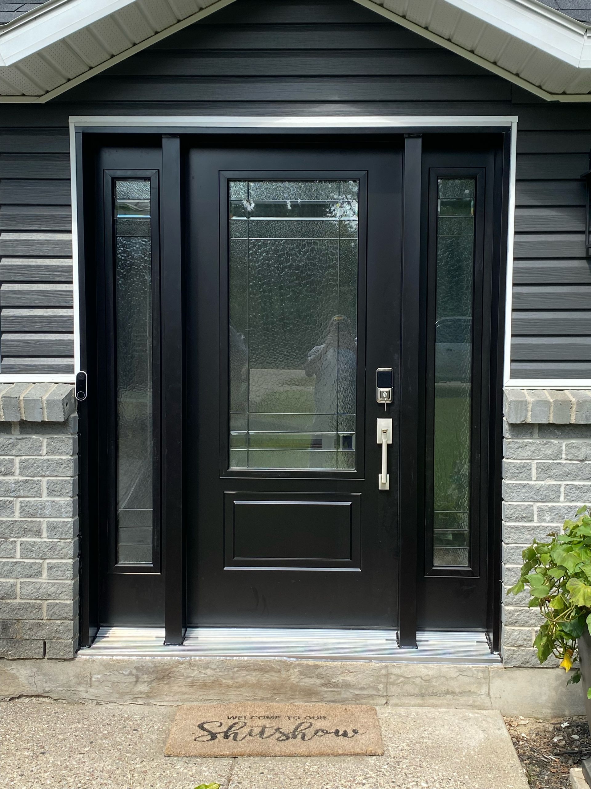 Black front entry door with sidelights on a gray brick and siding house exterior