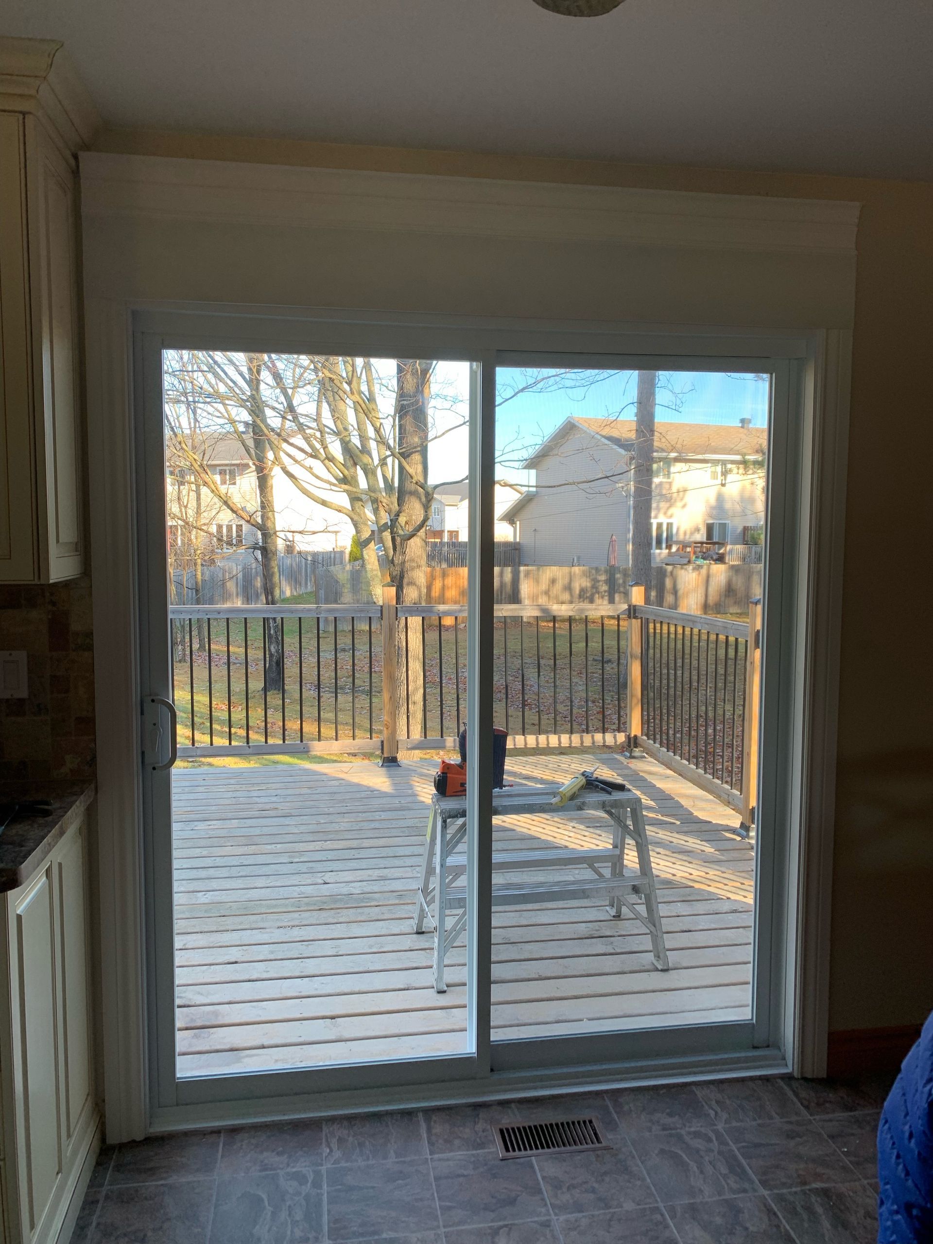 Sliding glass door to a snowy deck with two chairs and a backyard fence in the sunlight