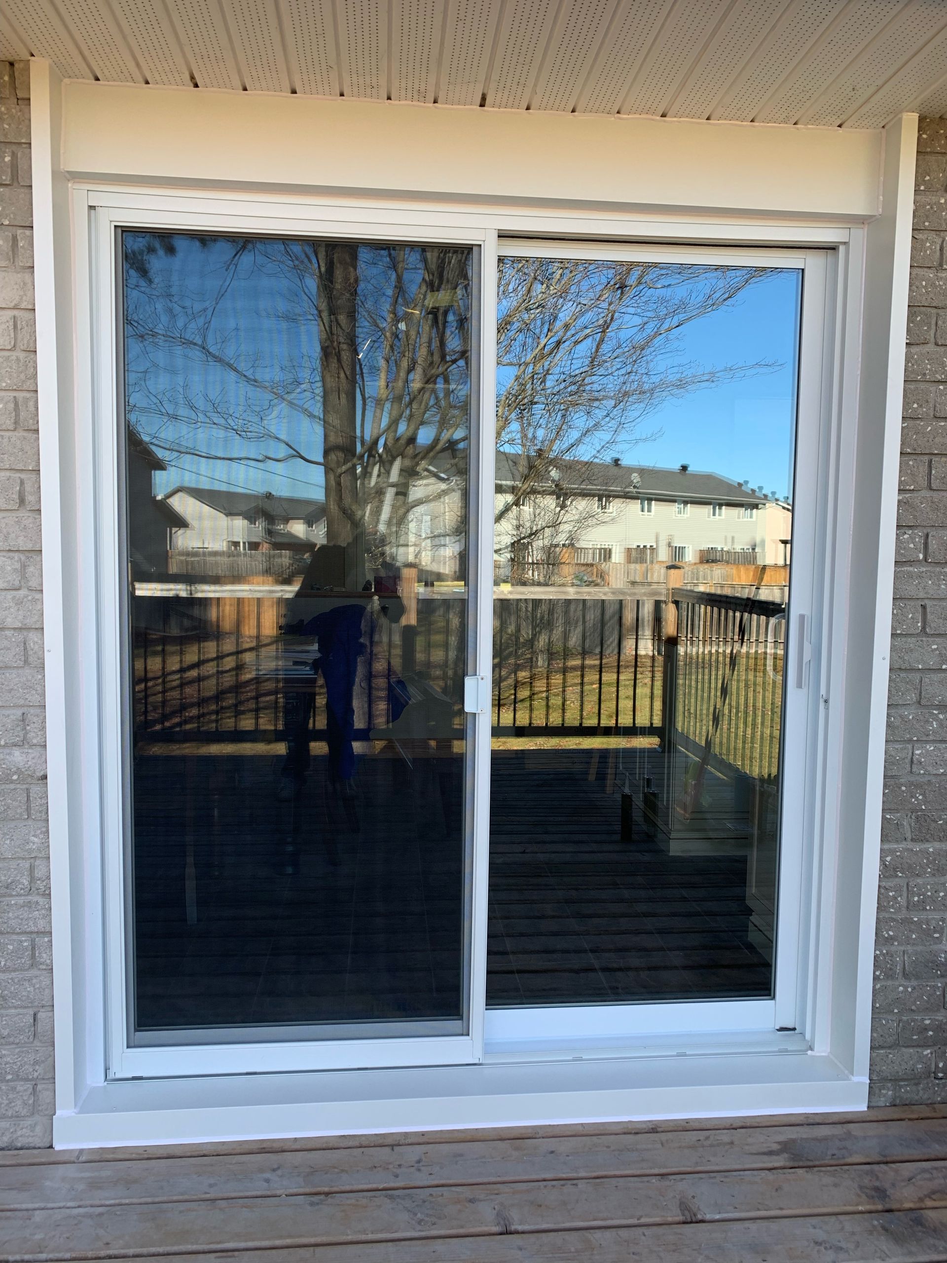Sliding glass patio door with white frame reflecting a backyard and neighboring homes.