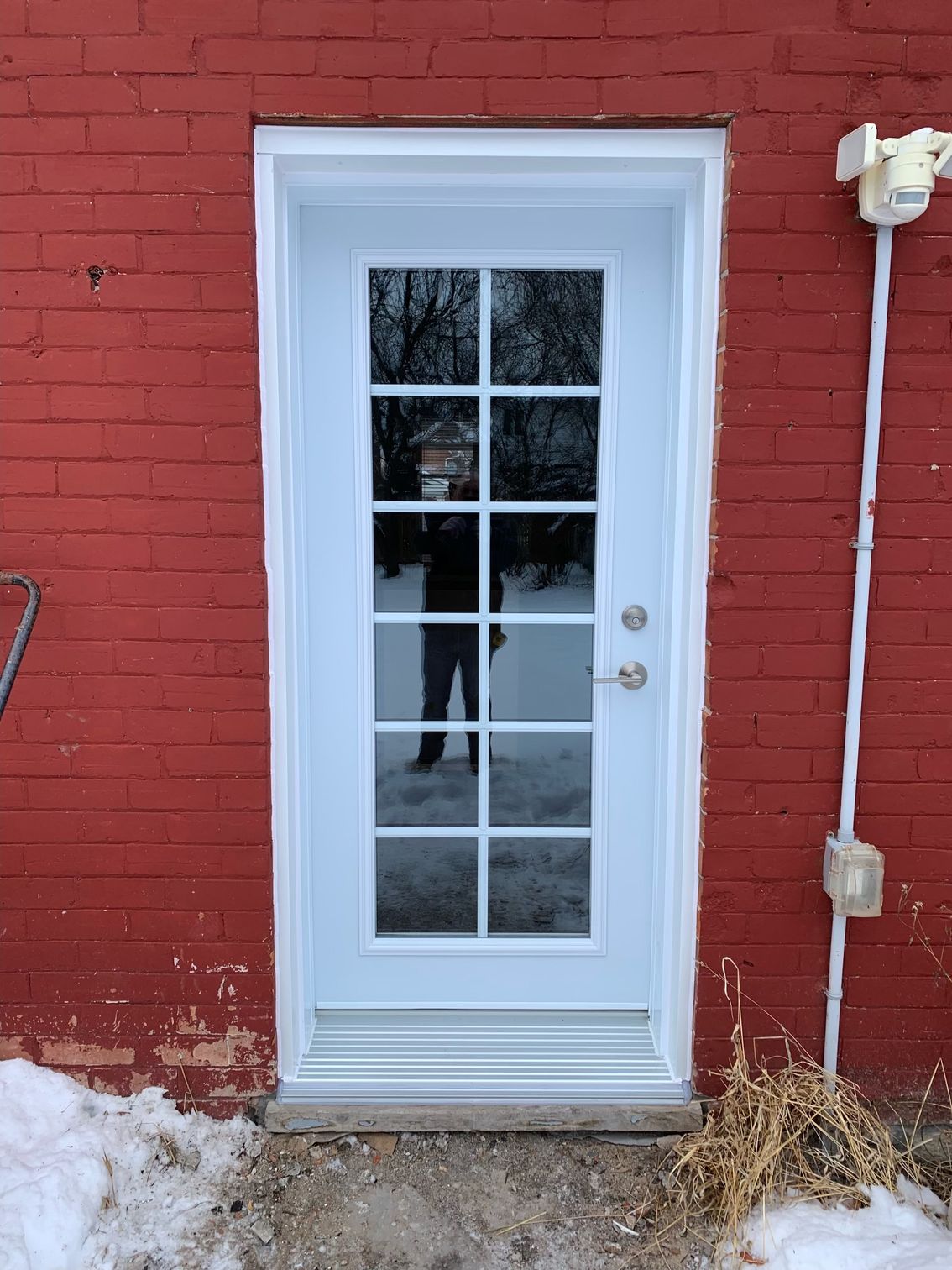 White glass-paned door set in a red brick wall, with snow on the ground.