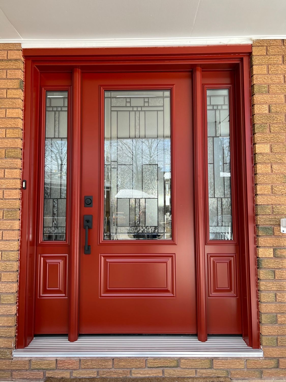 Red front double doors with glass panels and sidelights in a brick entryway