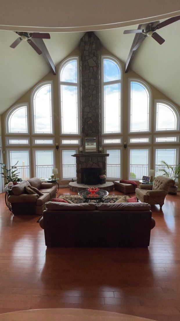 Spacious living room with a vaulted ceiling, large arched windows, fireplace, and dark wood flooring.