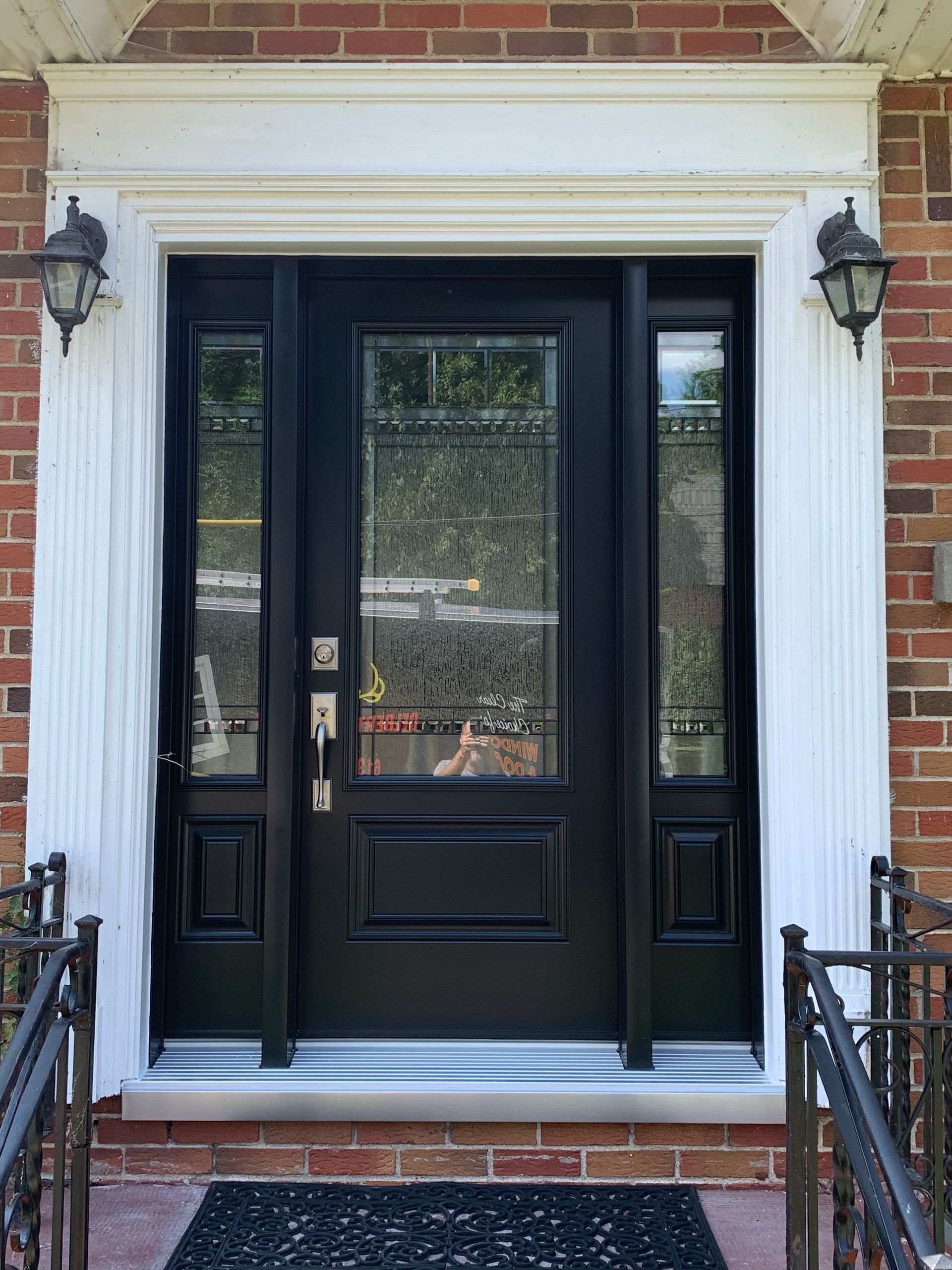 Black front door with sidelights and white trim on a brick house entrance
