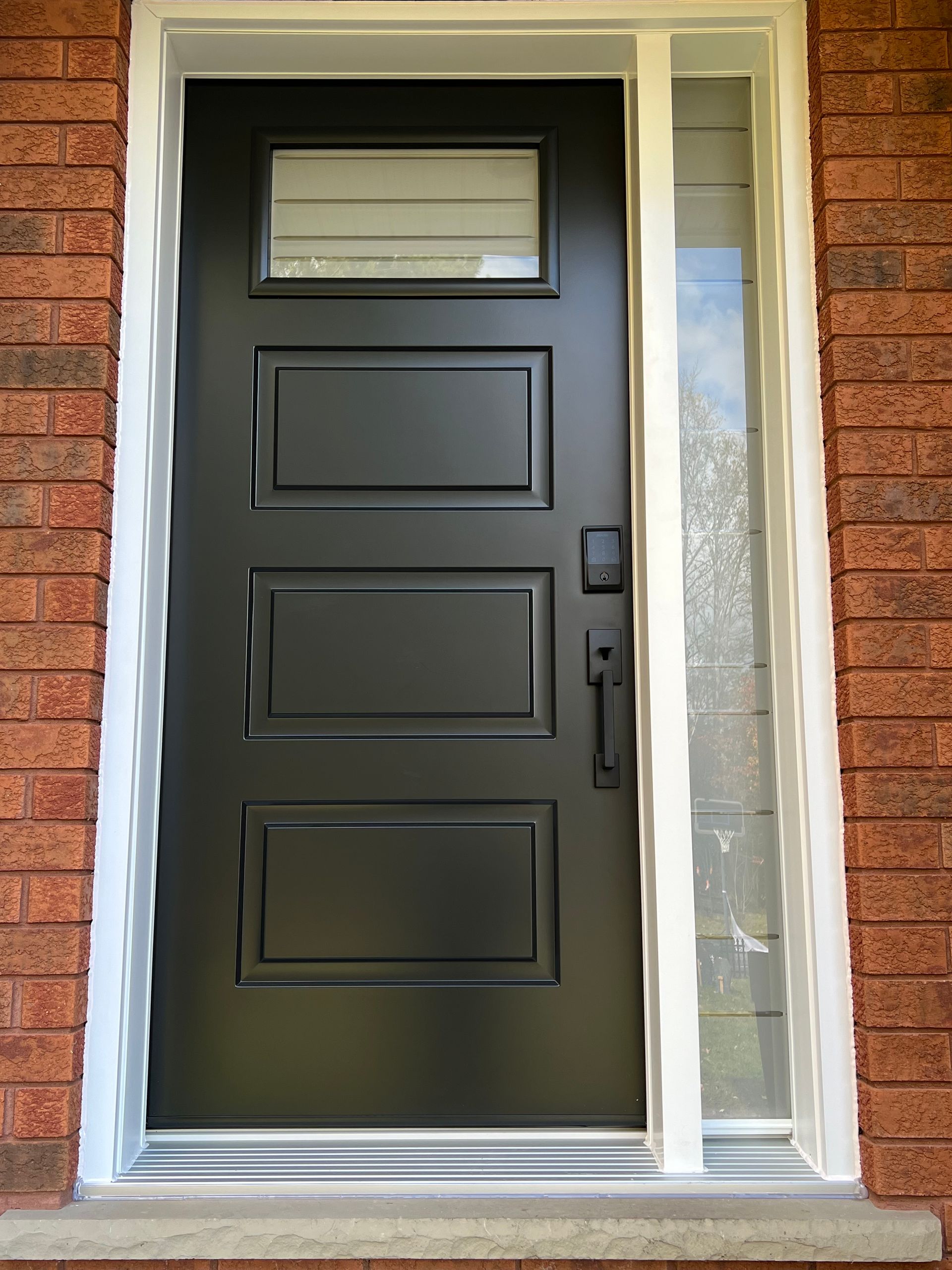 Black front door with window panel in a brick entryway