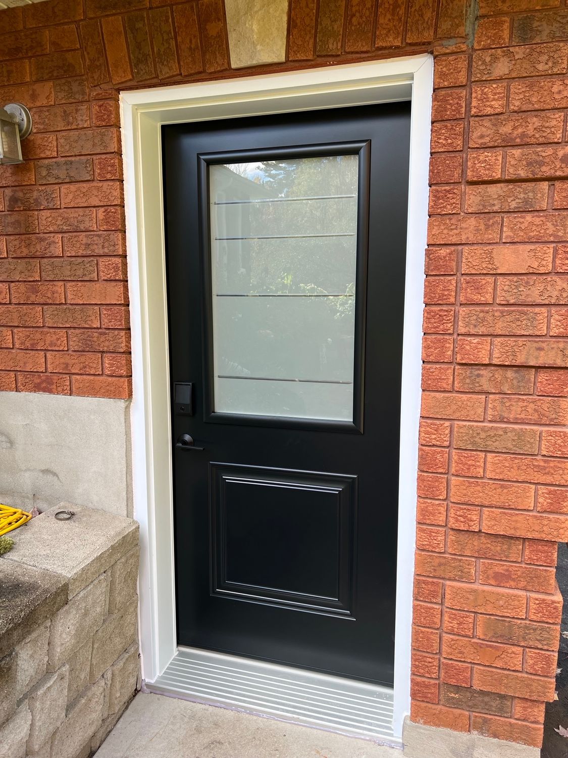 Black front door with frosted glass panel set in a brick exterior wall.