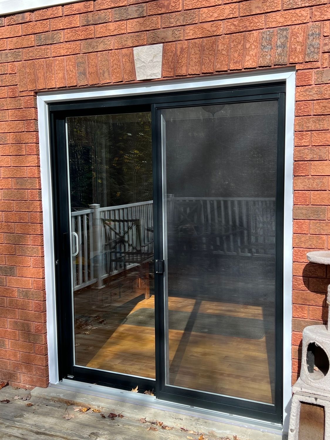 Sliding glass patio door with black frame in a red brick wall, reflecting an outdoor deck.