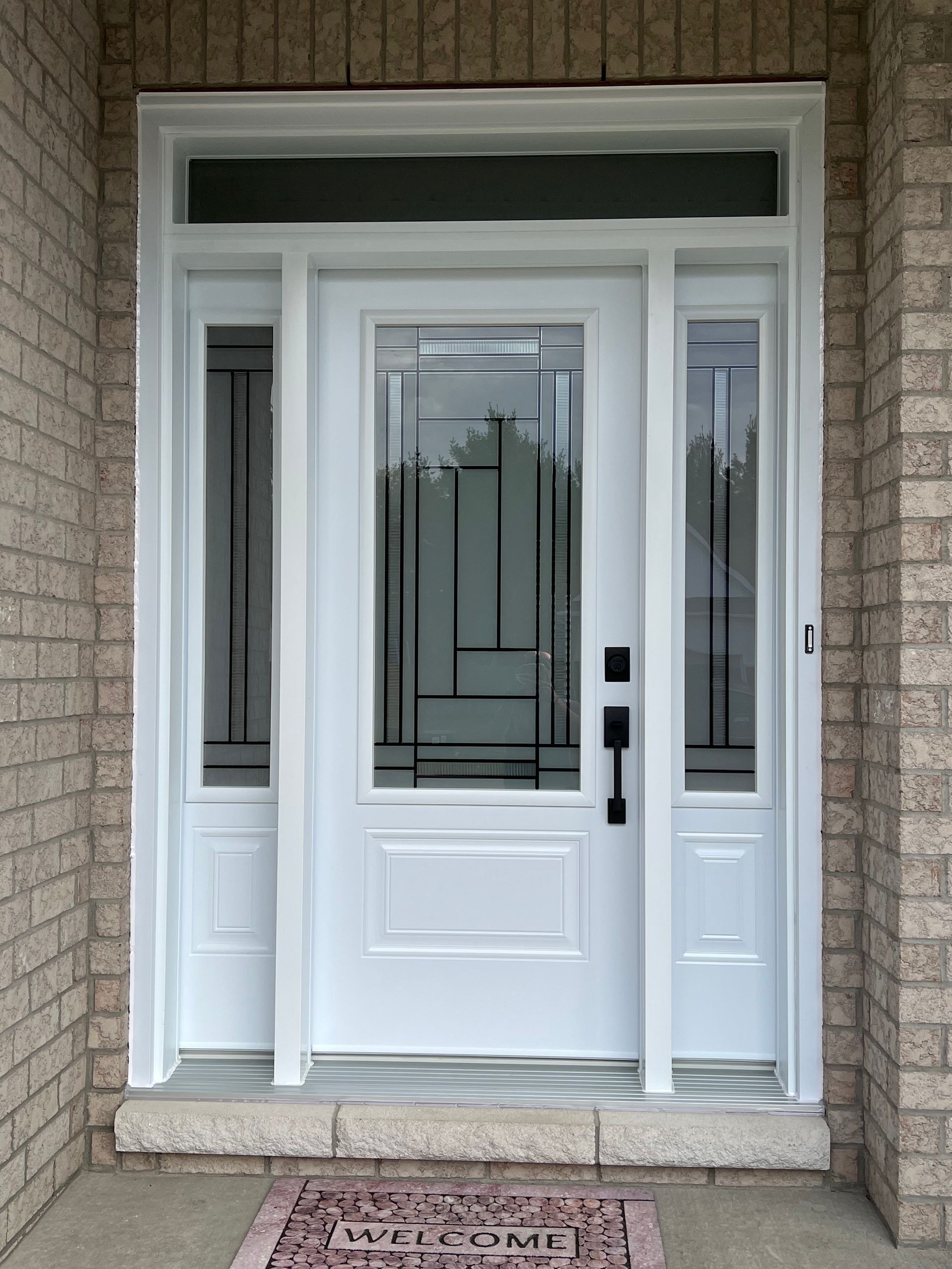 White front door with sidelights and transom window in a brick entryway
