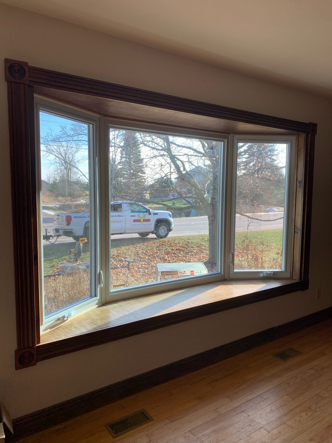 Sunlit bay window with dark wood trim overlooking a driveway and white pickup truck outside