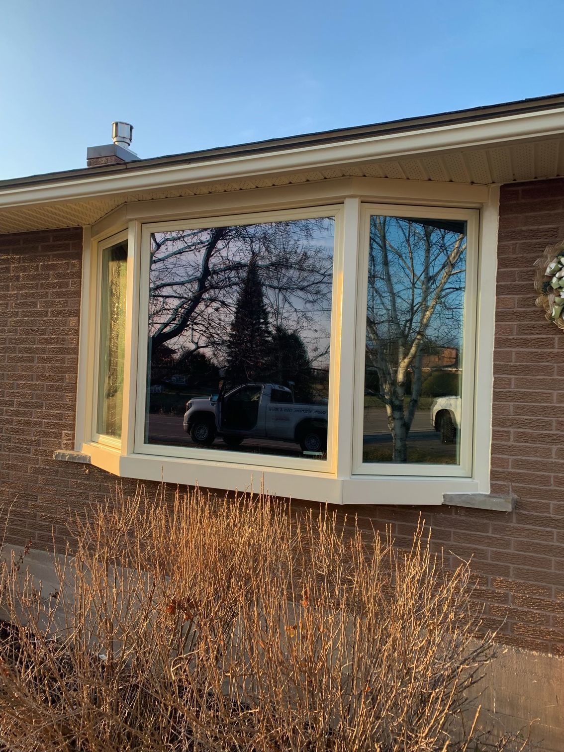 Brick house exterior with a beige bay window reflecting trees and a parked car.