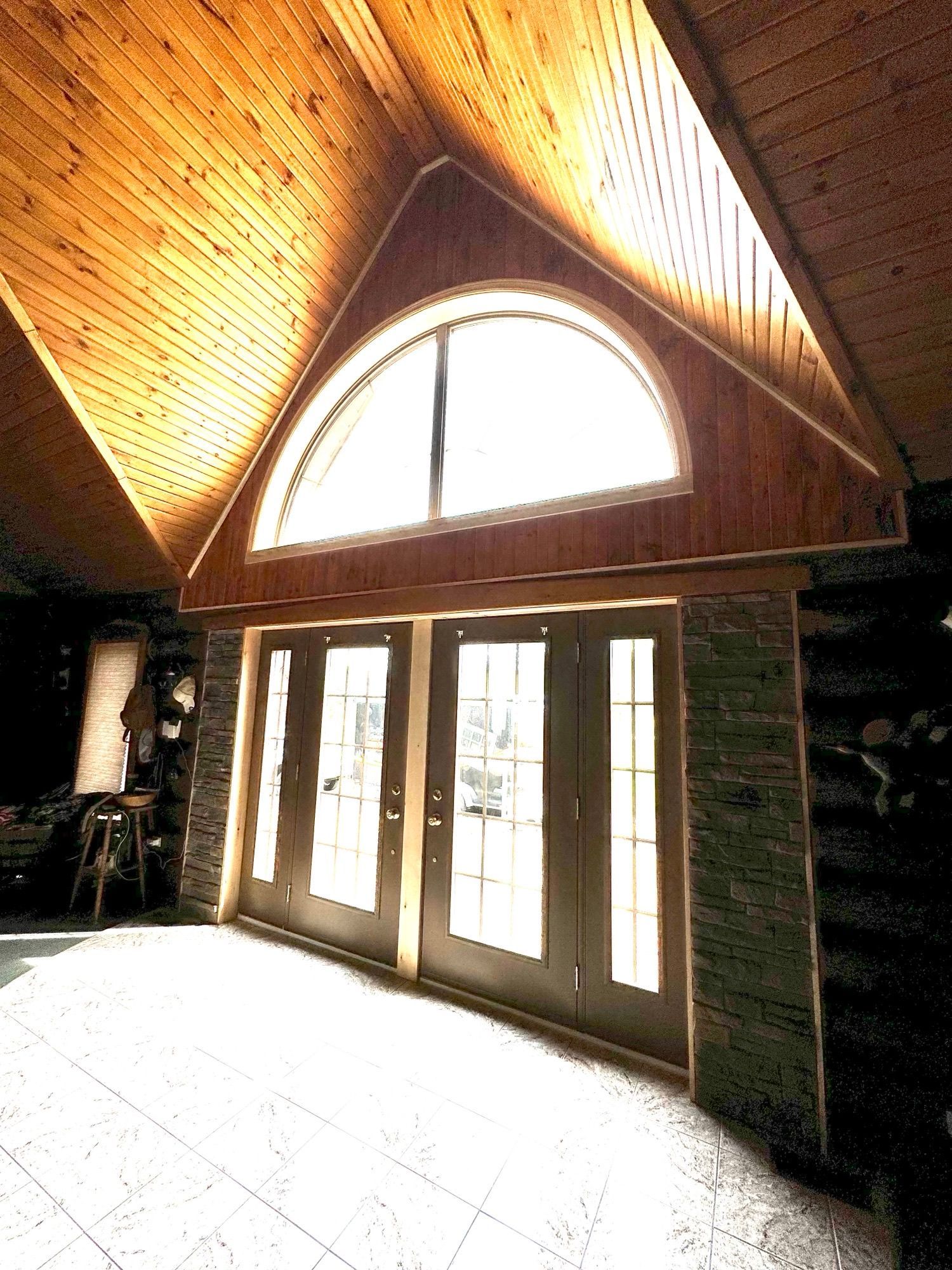 Interior with vaulted wood ceiling, arched window, and French doors in a bright rustic room