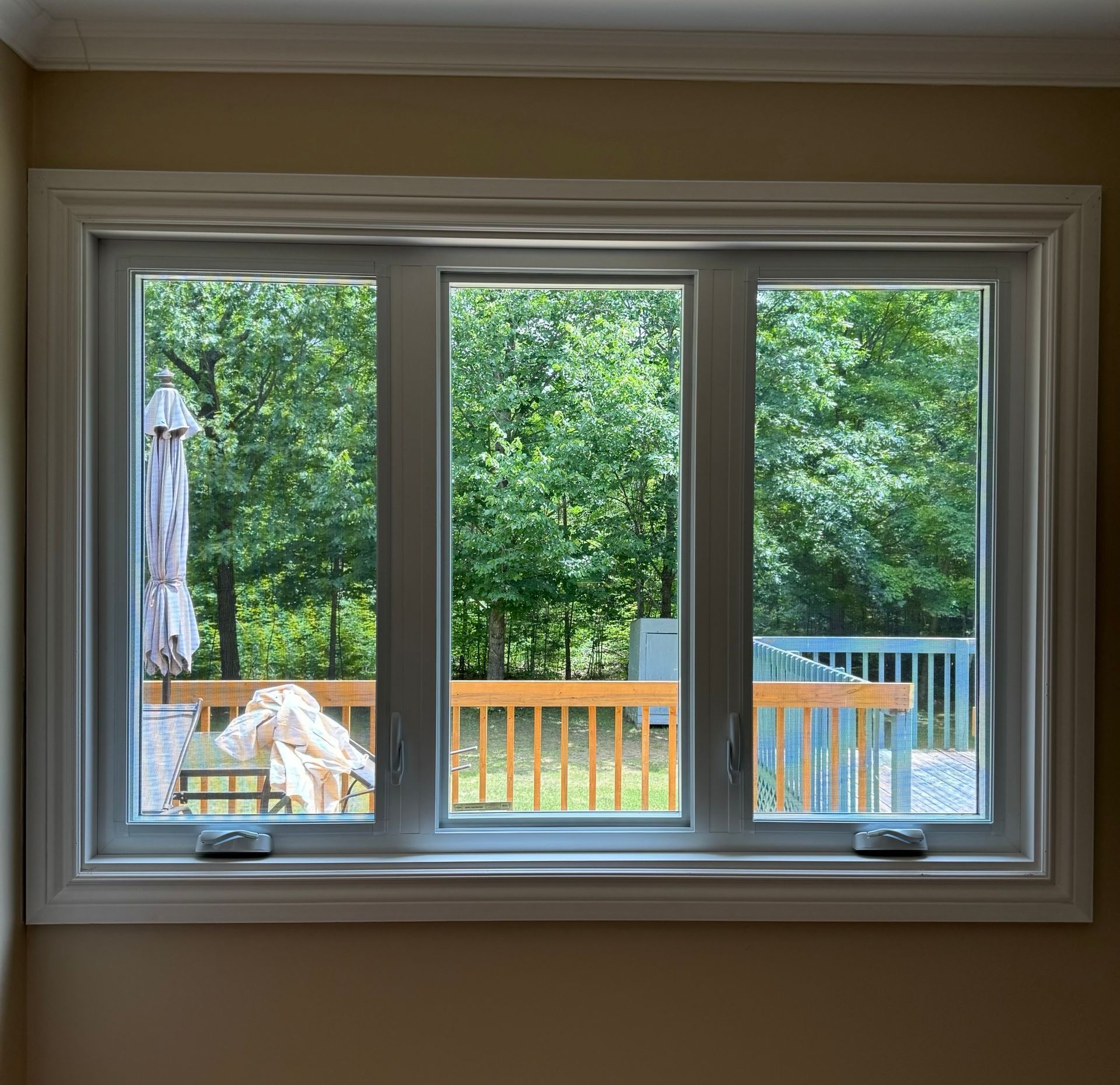 Window view of a backyard deck with trees, railing, and a closed patio umbrella