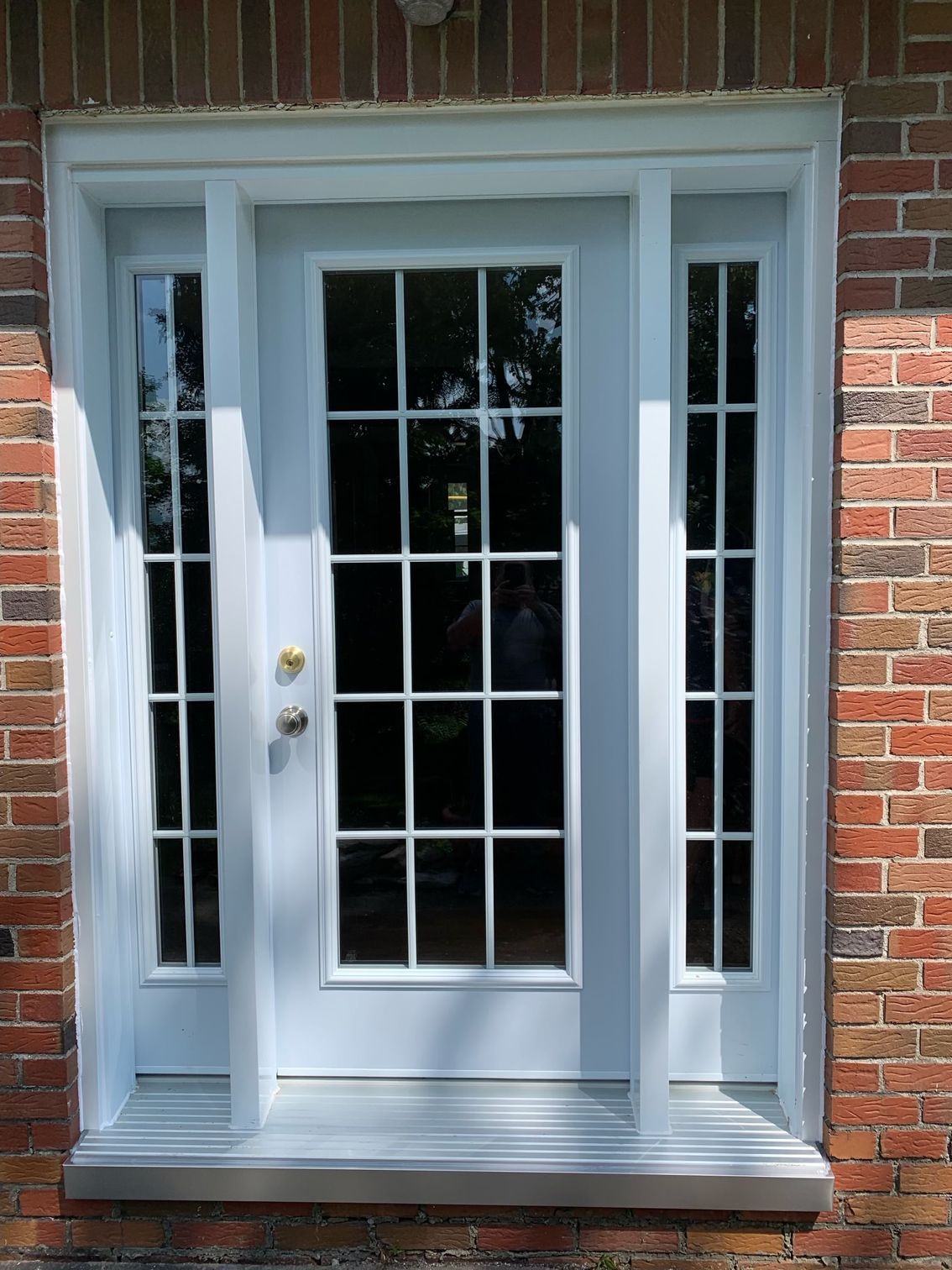 White front door with glass panes and sidelights set in a red brick wall
