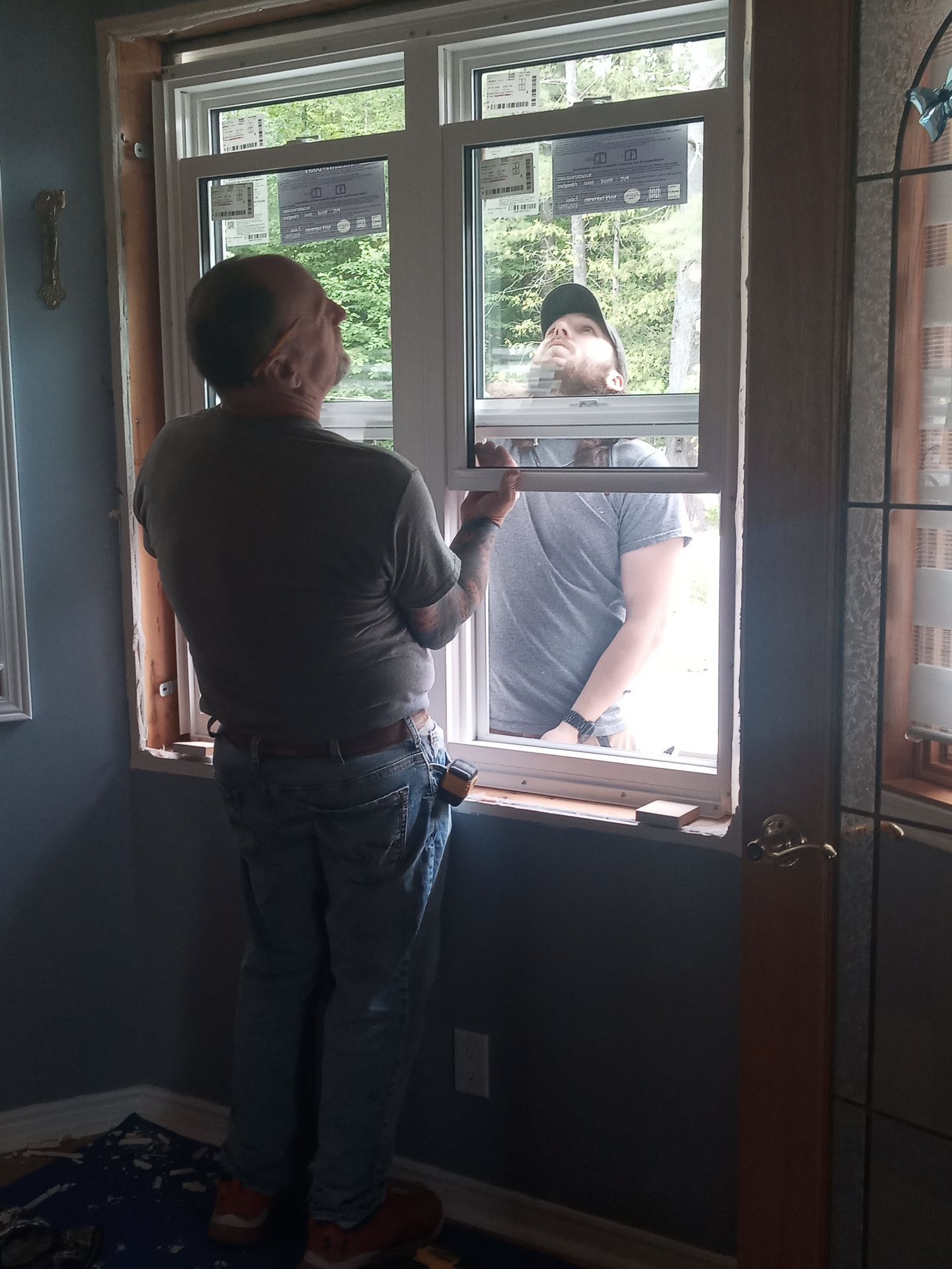 Two people installing a window frame inside a room with blue walls