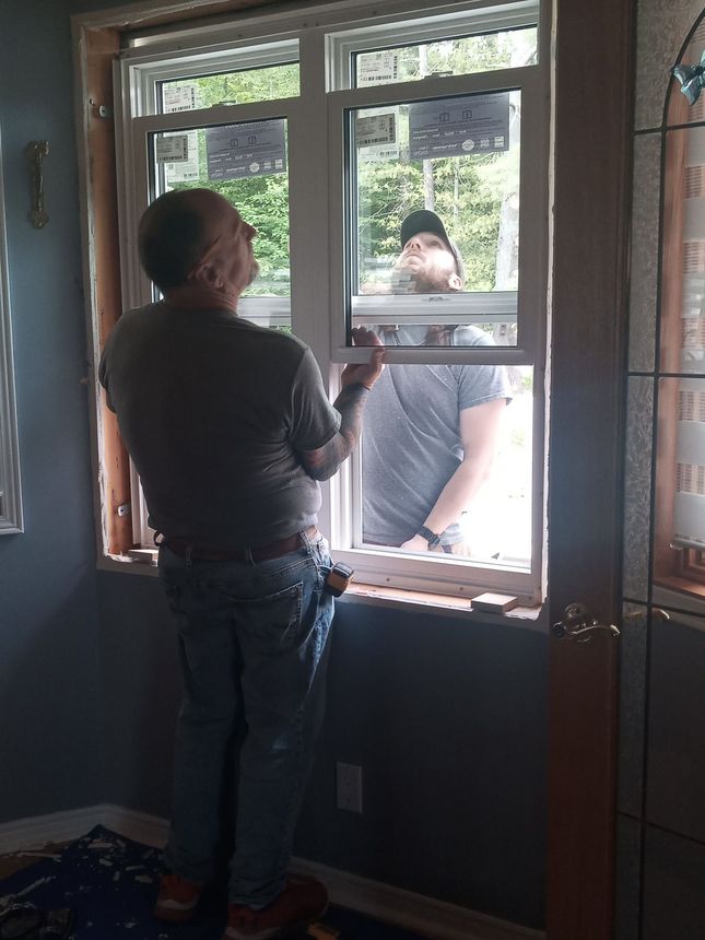 Two people installing a window frame inside a room with blue walls